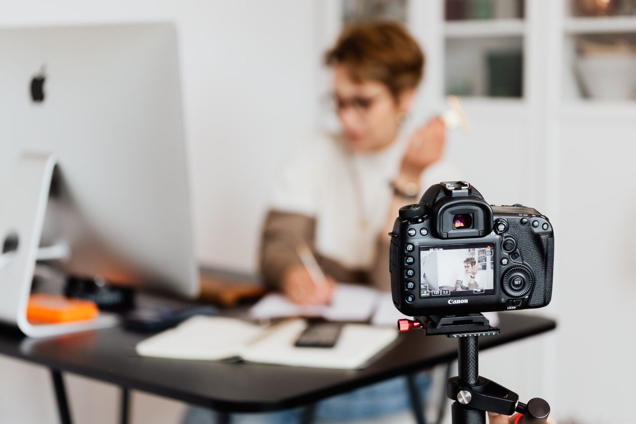 our-story Unrecognizable blurred lady working at table in modern office against photo camera placed on tripod